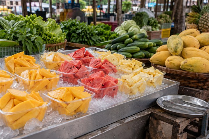 市場に並ぶ生野菜と、氷で冷やしたカットフルーツのイメージ(AI生成)