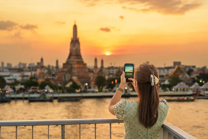 夕暮れのワットアルンを対岸からスマートフォンで撮影する旅行者